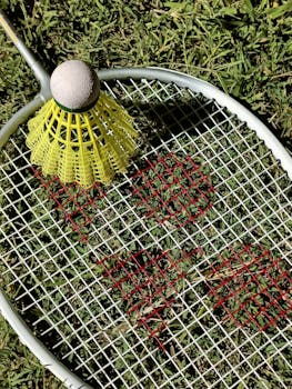 Close-up of a badminton shuttlecock on a racket on grass, highlighting sports equipment.