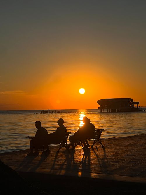 Free Silhouettes of people sitting on benches by the sea during a stunning sunset in Durrës, Albania. Stock Photo