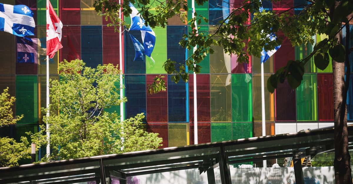 Vibrant glass building with Canadian and Quebec flags in downtown Montreal.