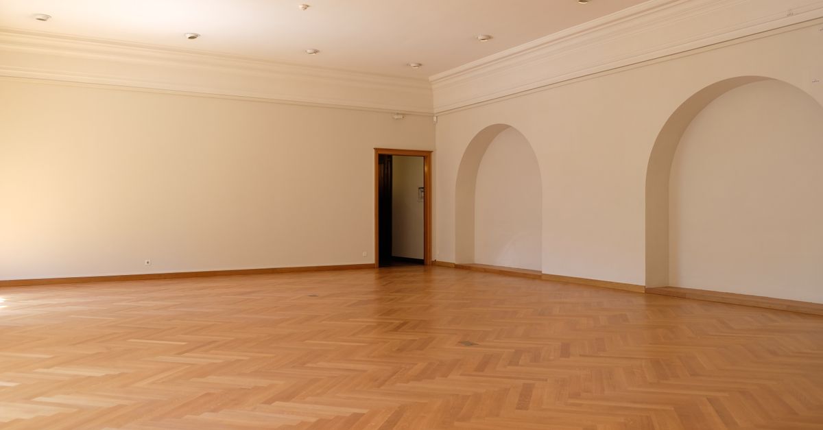 A large empty room with elegant wooden flooring, arches, and natural lighting, perfect for interior design inspiration.