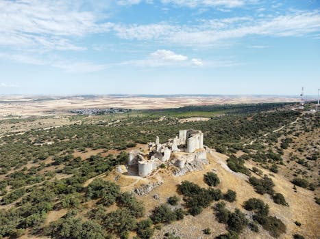 A drone captures the scenic ruins of a castle amidst the natural landscape of La Mancha, Spain.