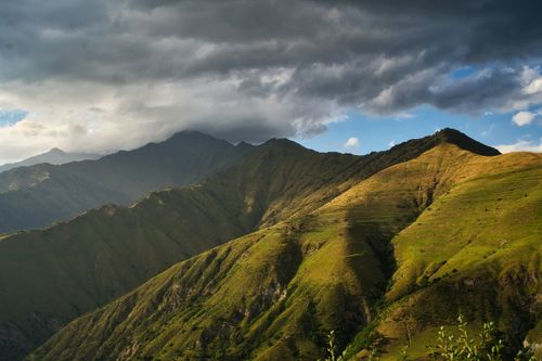 Free A stunning view of green hills and mountains under a dynamic cloudy sky, showcasing the beauty of nature. Stock Photo