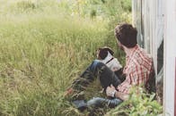 一名穿着格子衬衫的男子和他的狗坐在草地上，在户外享受着平静的一天