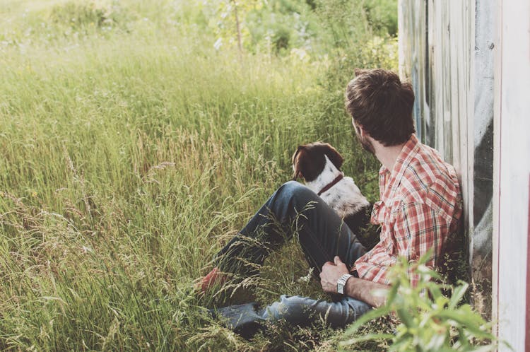 Man Sitting On Grass Beside Dog