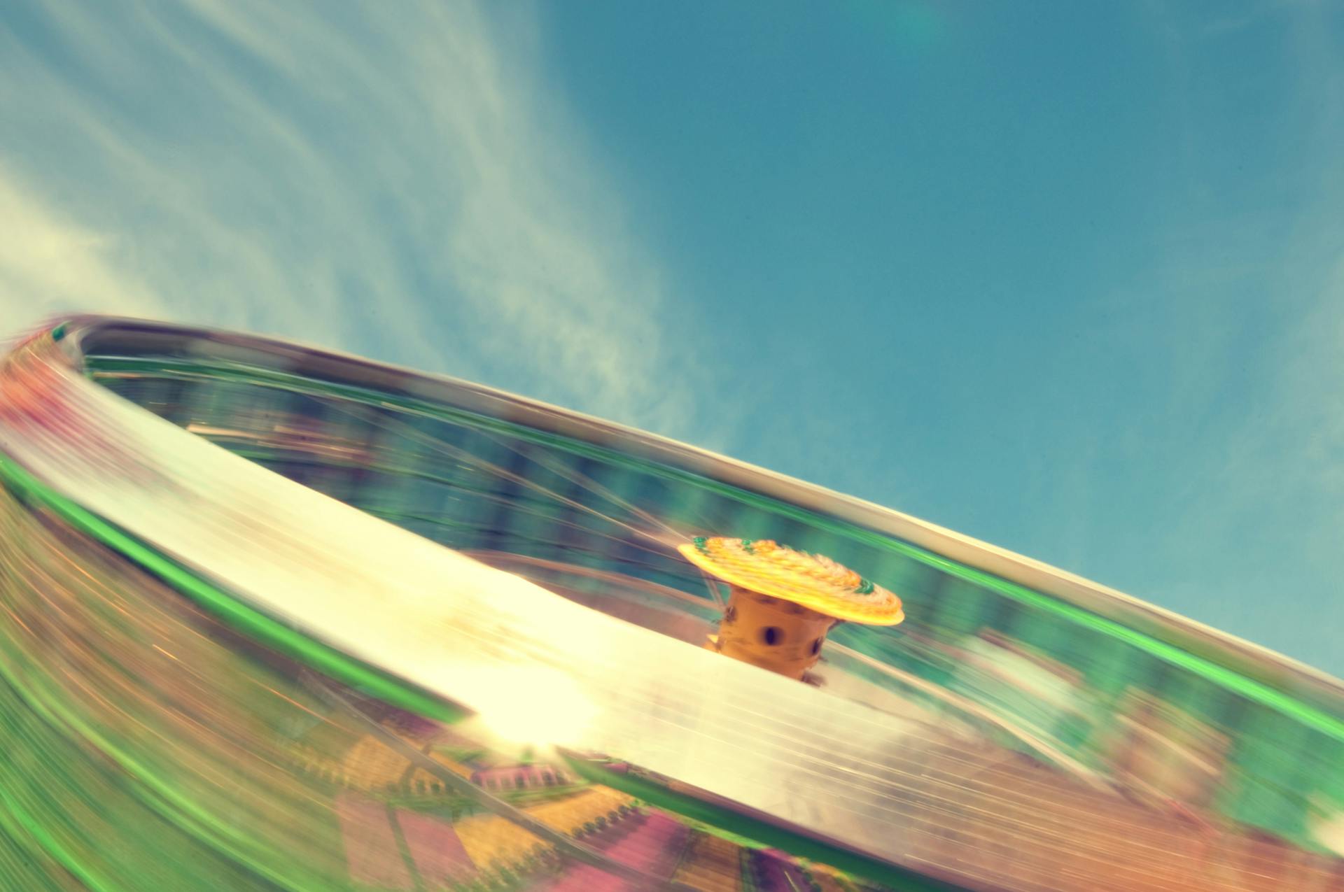 Dynamic long exposure capture of a colorful carnival ride against a bright blue sky.