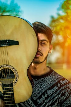 Portrait of a young man with an acoustic guitar outdoors during sunset, showcasing vibrant colors and musical expression.