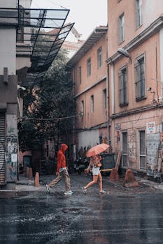 Couple walking with an umbrella on a rainy day in a narrow city street with wet buildings.