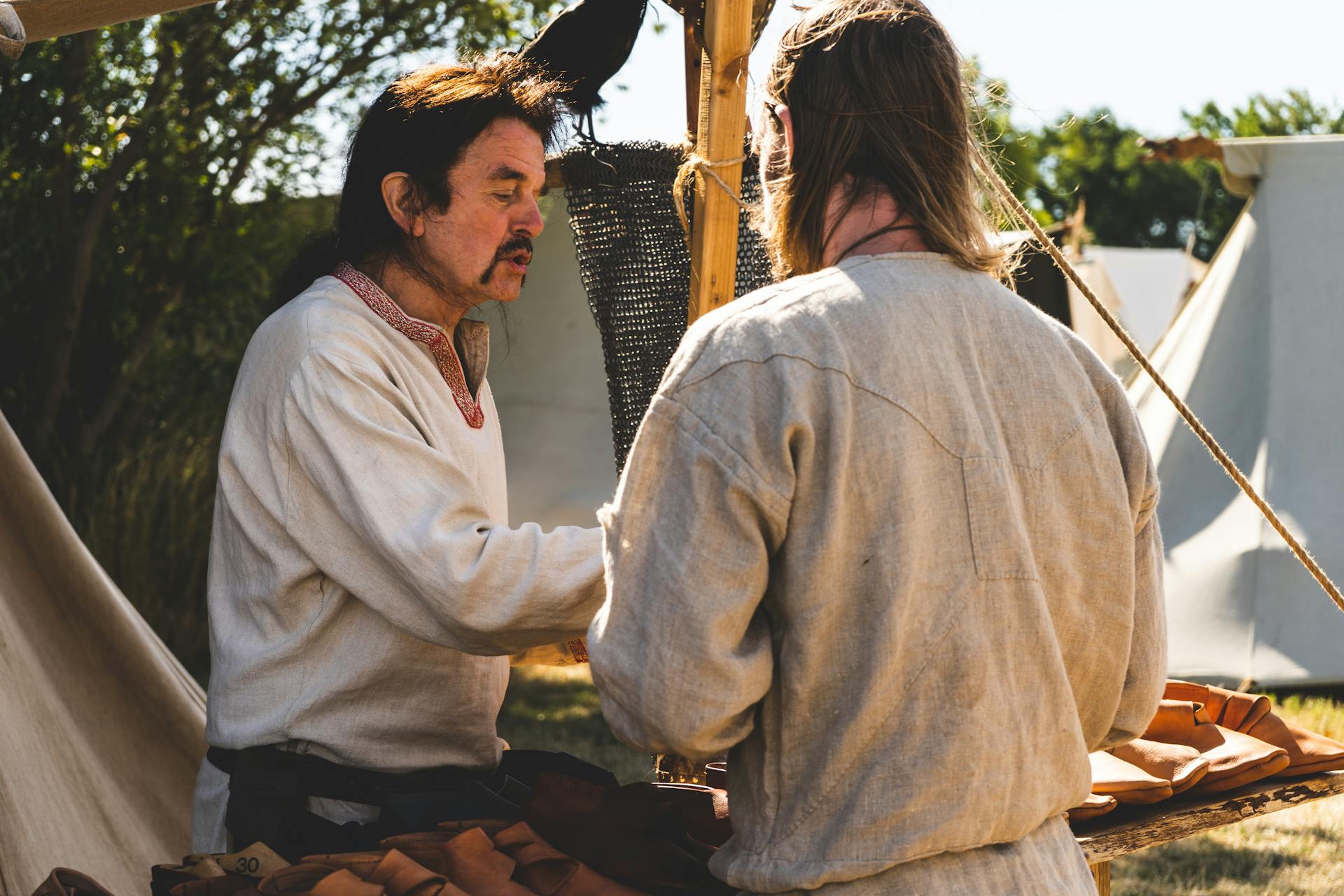 Two men engage in historical trade at a rustic outdoor medieval market.