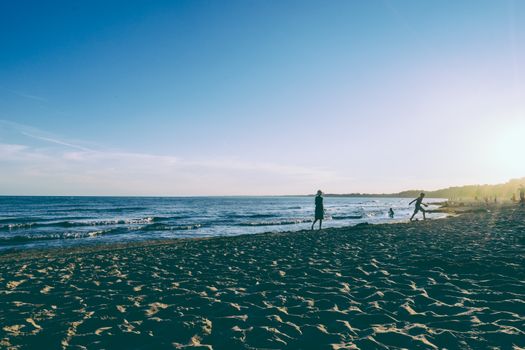 People enjoying the beach at sunset with waves and a sunlit sky, creating a peaceful atmosphere.