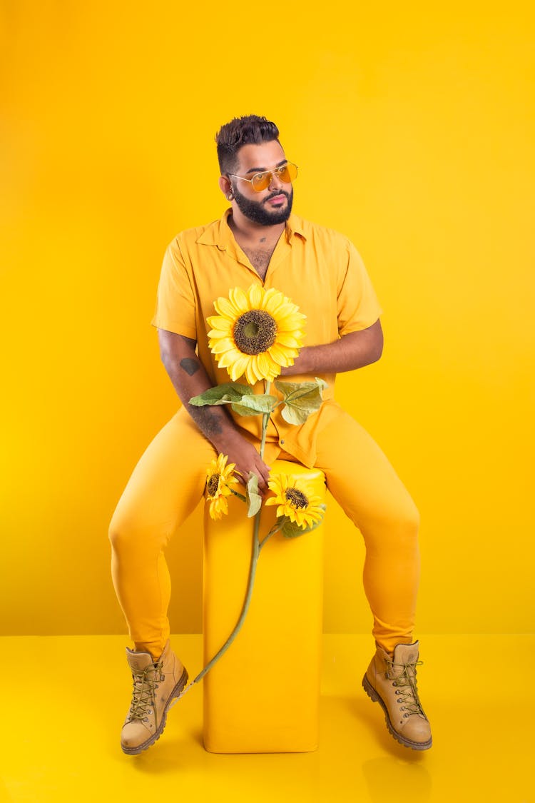 Man In Yellow Clothes Posing With Sunflowers In Studio