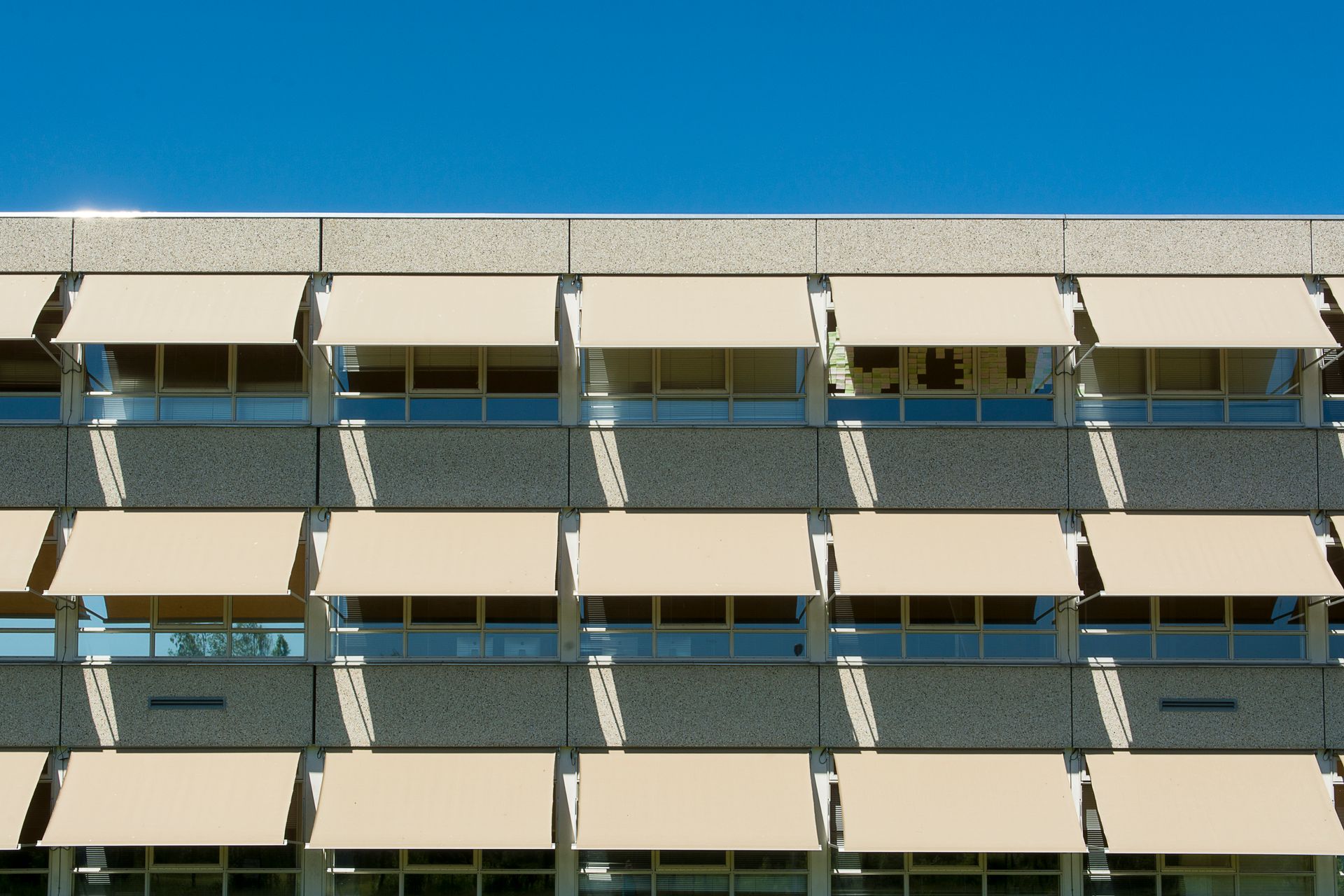 Facade of a modern residential building with sun shades under a clear blue sky.