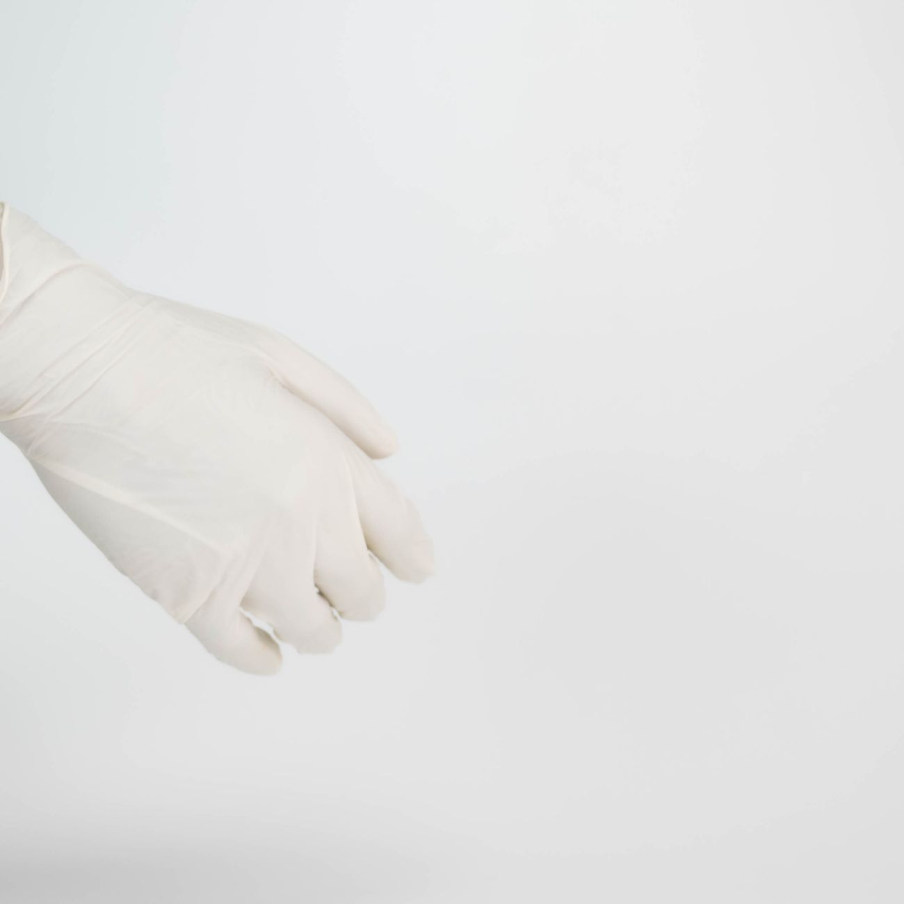 Close-up of a hand wearing a white latex glove against a plain white background.