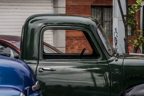 Free Close-up of a classic green GMC truck parked on a street in an urban setting. Stock Photo