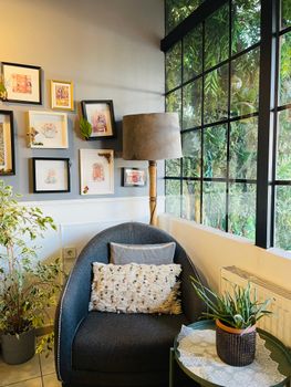 Inviting corner with armchair, indoor plants, and wall art by a window, perfect for relaxing.