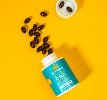 Close-up of NuHemp CBD capsules spilling on a bright yellow background.