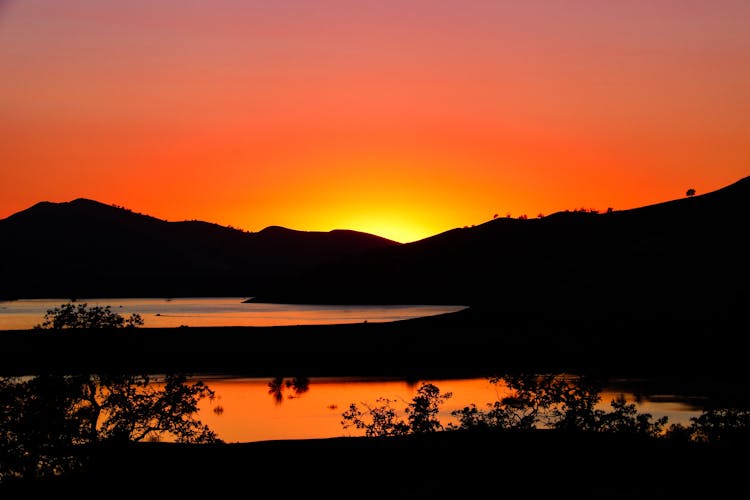 Two Lakes Surrounded By Silhouettes Of Hills At Sunset