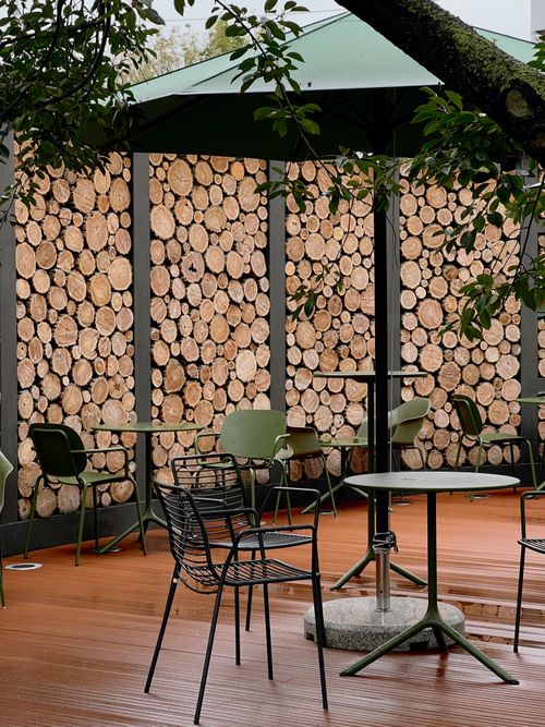 Free Cozy outdoor café setting with rustic wood stack walls, green tables, and chairs under an umbrella. Stock Photo