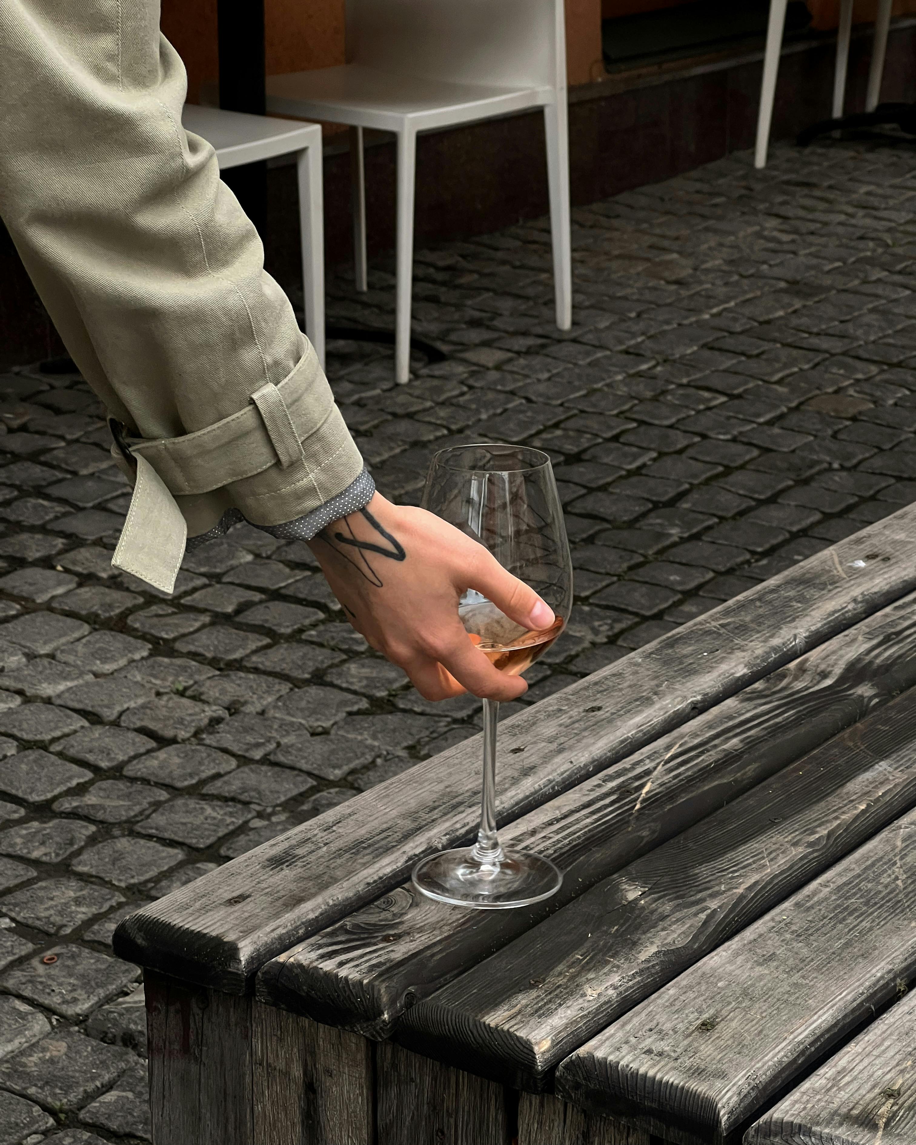 A person elegantly places a white wineglass on a weathered wooden table outdoors.