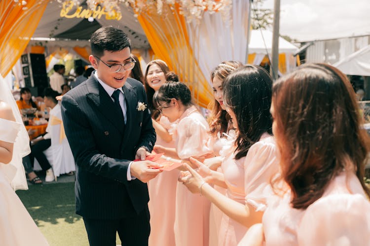 Man In Black Suit Handing Out Red Envelopes To Women