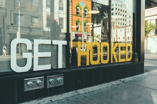 Street scene with a reflection on a glass storefront displaying a 'Get Hooked' sign.