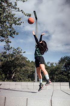 Female athlete joyfully playing basketball outdoors in a sunny park setting.