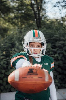 Close-up of a female football player in uniform posing with the ball outdoors.