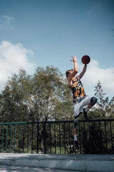 Athlete jumps high to make a basketball shot against a clear sky in Ciudad de México park.