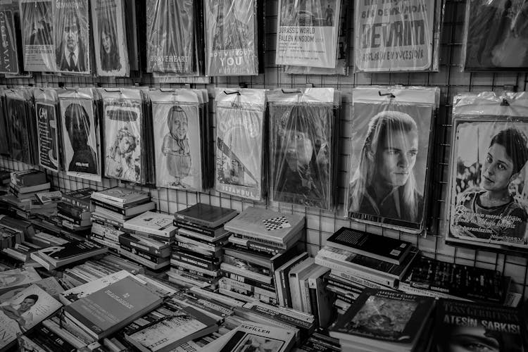 Grayscale Photo Of Book Stack Beside Posters