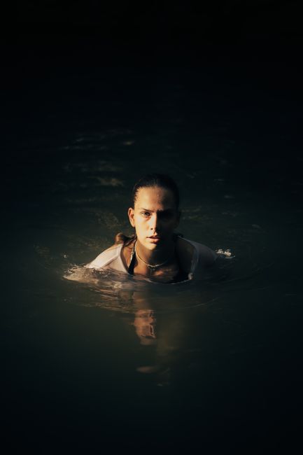A serene portrait of a woman swimming in a dark lake at night, with soft lighting.