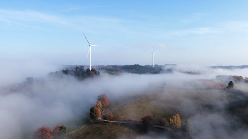 An Aerial Photography of a Windmills Between Trees Under the Blue Sky and White Clouds