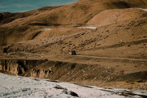 Free A solitary jeep traverses a barren mountain road in an arid landscape with rugged hills. Stock Photo