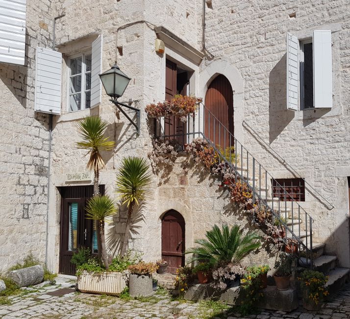Charming stone facade of a historic house in Trogir, Croatia featuring potted plants and classic architectural details.
