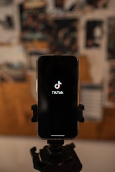 Close-up of a smartphone on a tripod displaying the TikTok app. Blurred background.