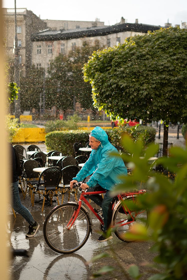 Man In Raincoat Riding Bike In Rain