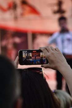 Person recording a live concert with a smartphone in a bustling outdoor setting.
