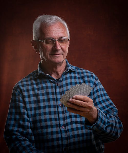 Close-Up Shot of an Elderly Man in Checkered Long Sleeves Holding Playing Cards