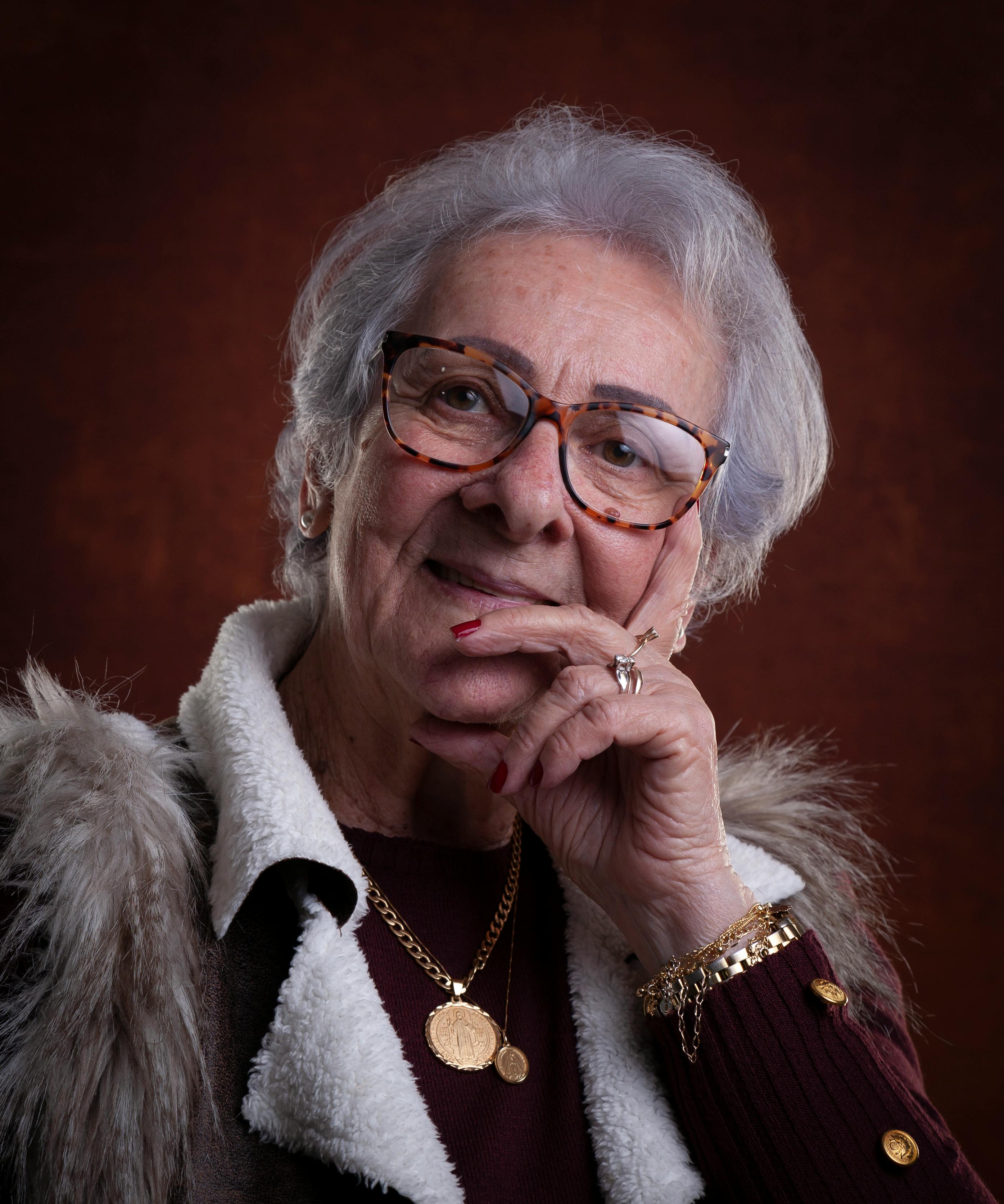 A sophisticated portrait of an elderly woman with eyeglasses and elegant jewelry.