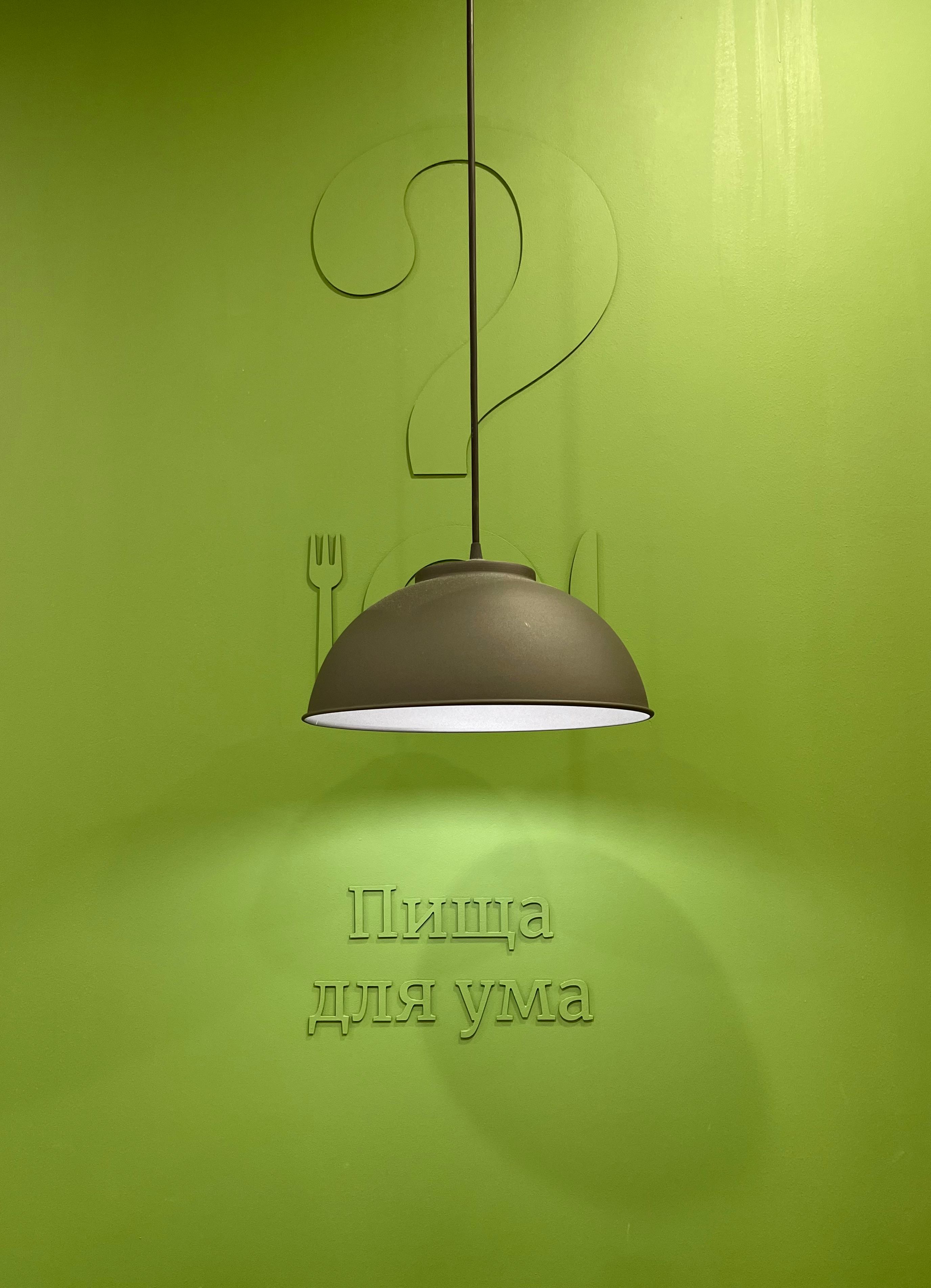 A minimalist pendant lamp on a vibrant green wall with subtle textured decoration.