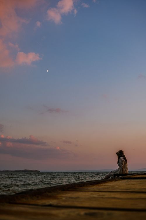 Free A woman sitting by the sea during sunset, capturing a tranquil moment with a moonlit sky. Stock Photo