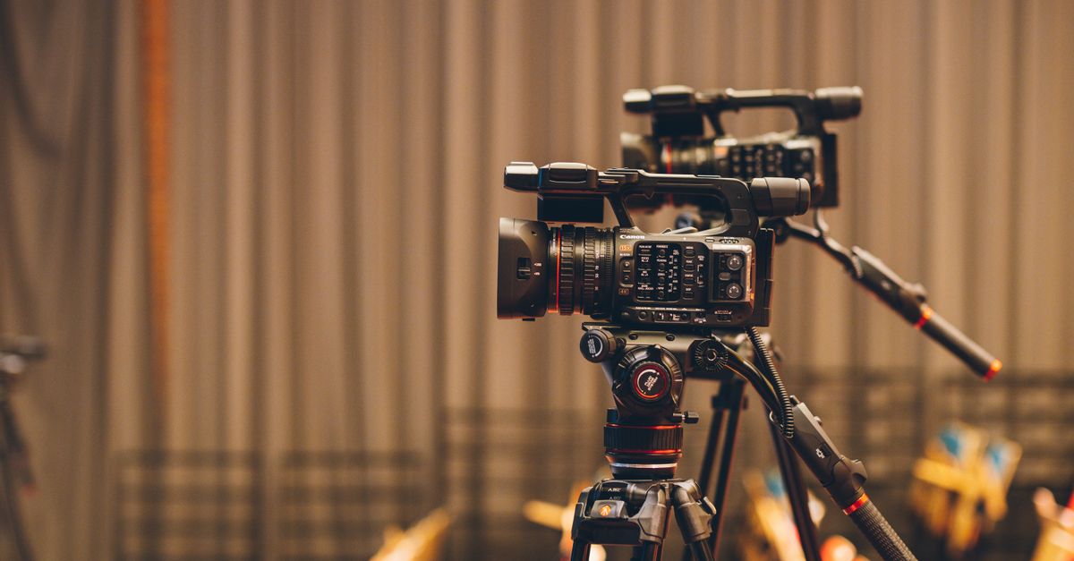 Close-up of professional video cameras on tripods, set up indoors for filming.