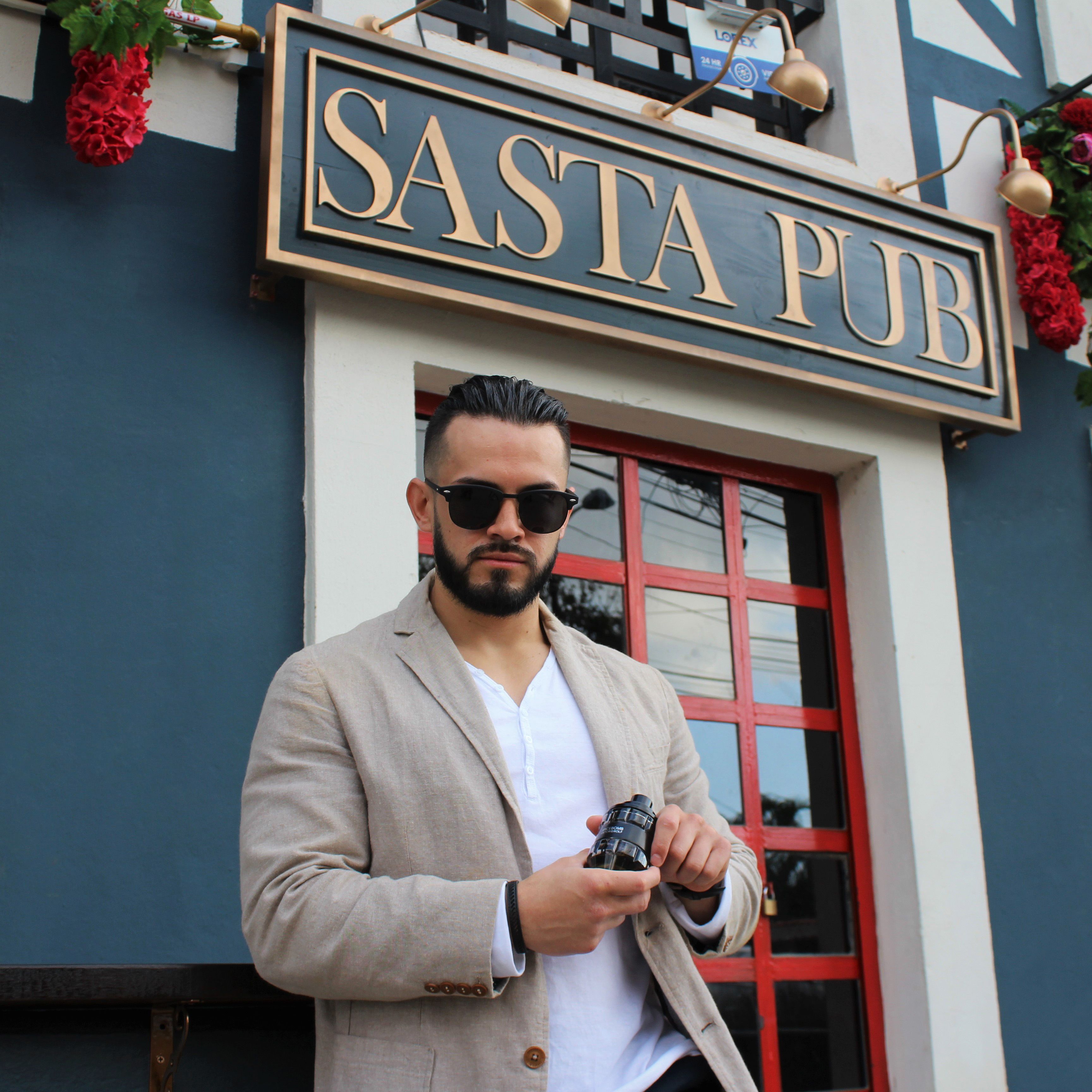 A fashionable man in sunglasses holds a camera outside a pub with a stylish exterior.