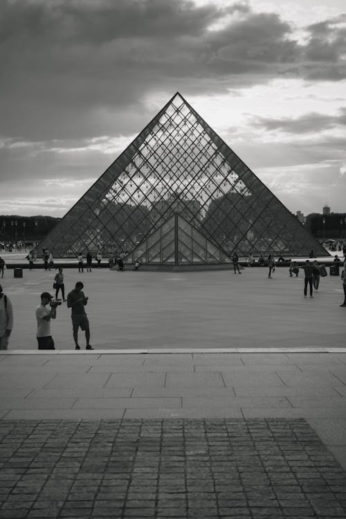 A Grayscale Photo of People Walking in Front of Louvre Museum