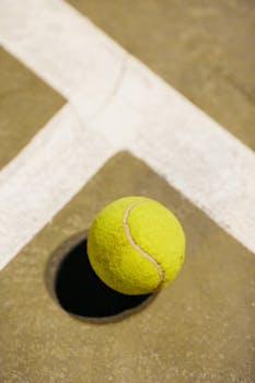 Detailed view of a tennis ball resting on a marked court surface, highlighting texture.