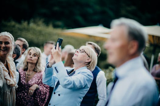 A senior woman takes a photo at an outdoor gathering with a smartphone.