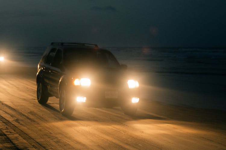 A Black Car Moving On The Beach Sand At Night