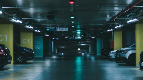 Free A dimly lit underground parking garage featuring parked vehicles and directional signs in Budapest. Stock Photo