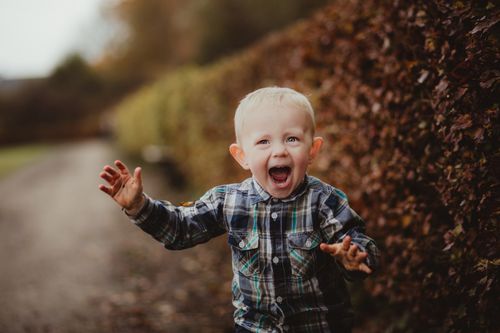 Free Energetic young child in plaid shirt expressing joy outdoors during fall season. Stock Photo