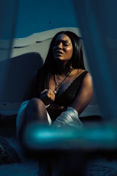 Dramatic portrait of a woman in black lingerie sitting alone with a solemn expression.
