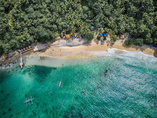 Free Stunning drone shot of a lush coastline with vibrant blue water and boats. Stock Photo