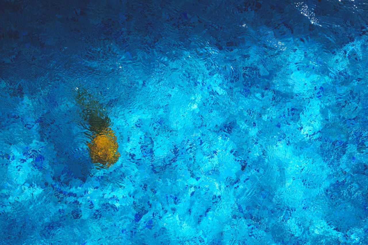 a pineapple submerged in a vibrant blue pool creates a tropical abstra